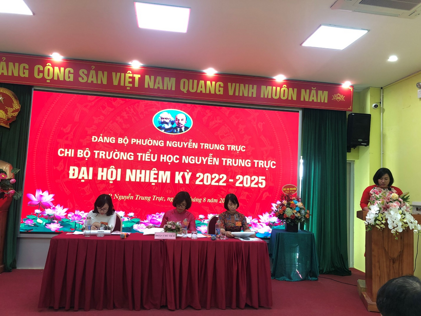A group of women sitting at a table with flowers in front of a red banner

Description automatically generated with low confidence