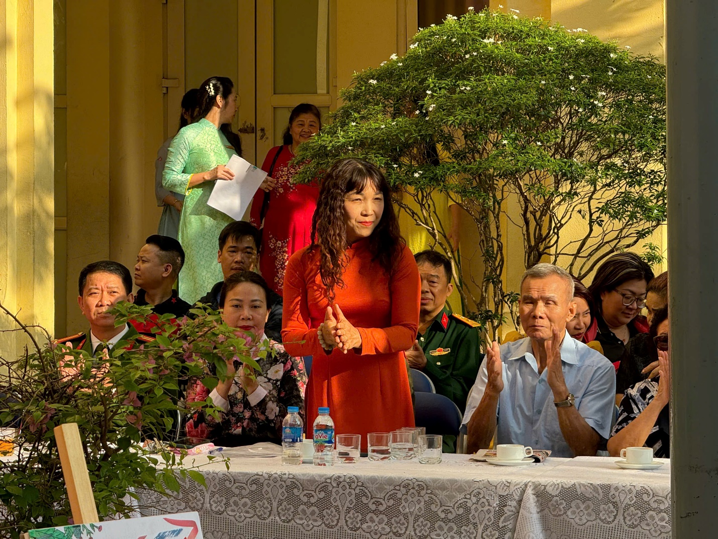 A person standing at a table with people in the background

Description automatically generated