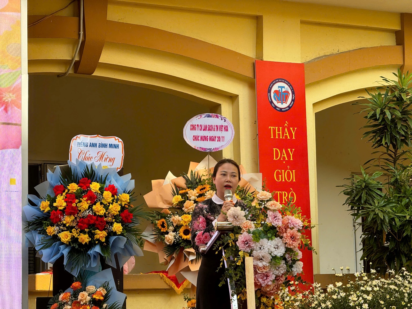 A person speaking into a microphone with flowers

Description automatically generated