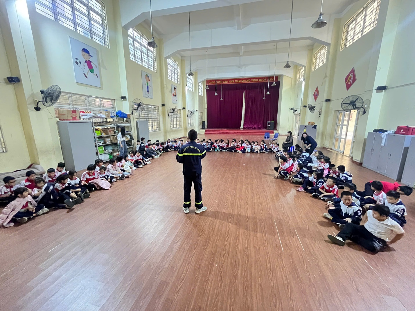 A group of children sitting on the floor in a room with a person standing in front of them

Description automatically generated