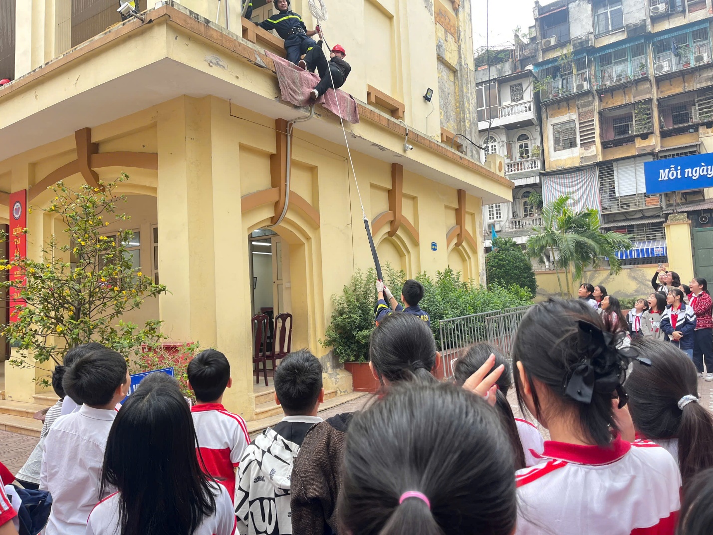 A group of people looking at a person climbing a building

Description automatically generated