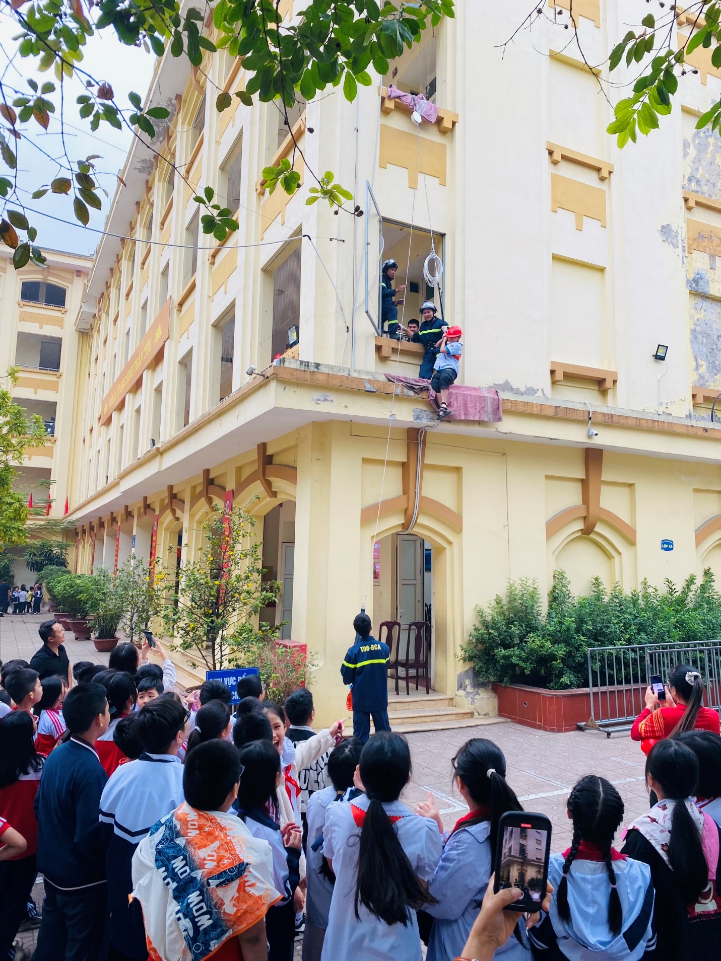 A group of people watching a person climbing a ladder on a building

Description automatically generated