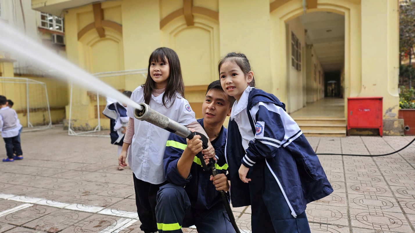 A person and two girls holding a fire hose

Description automatically generated