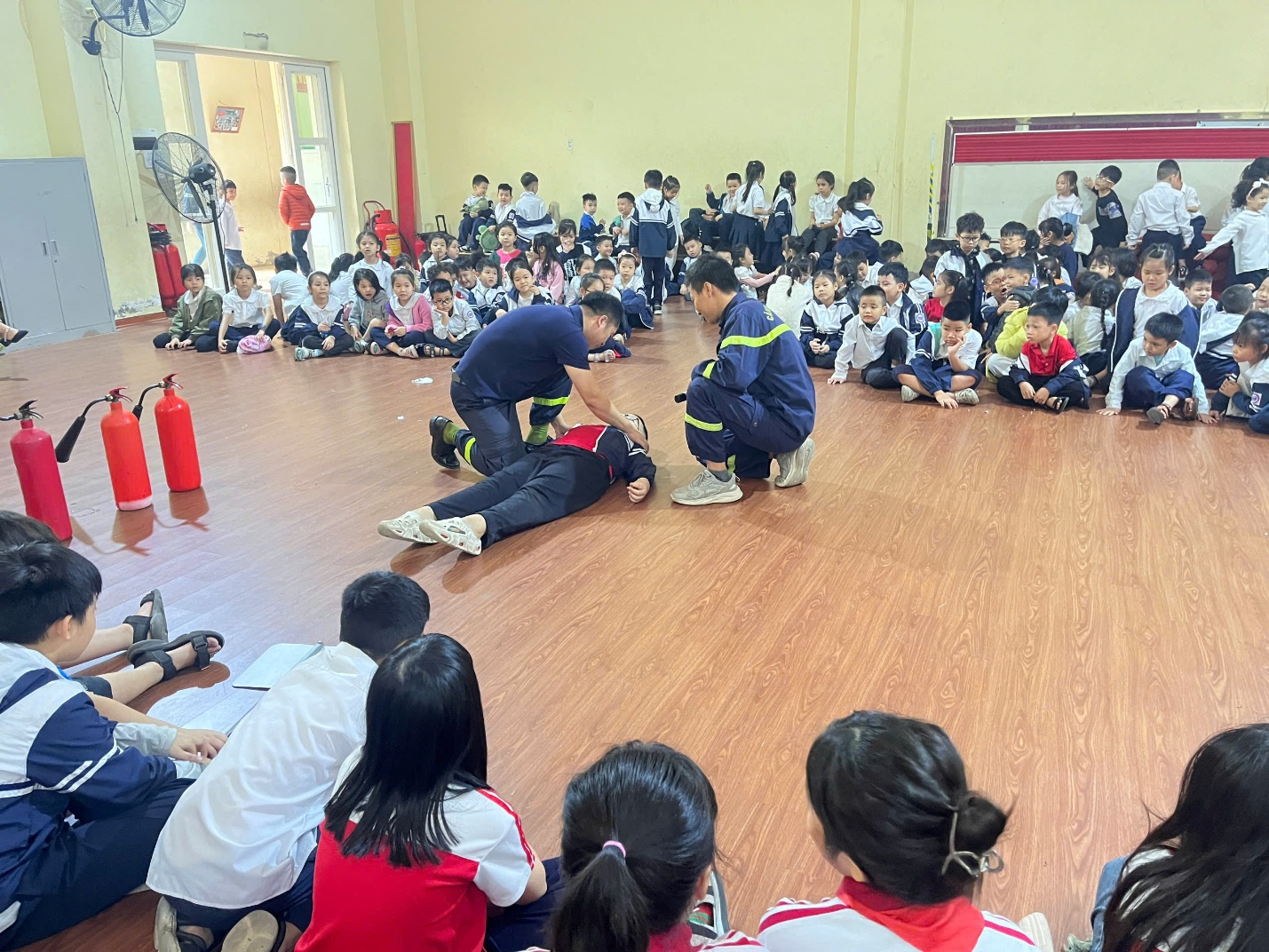 A group of people sitting in a room with a person lying on the floor

Description automatically generated