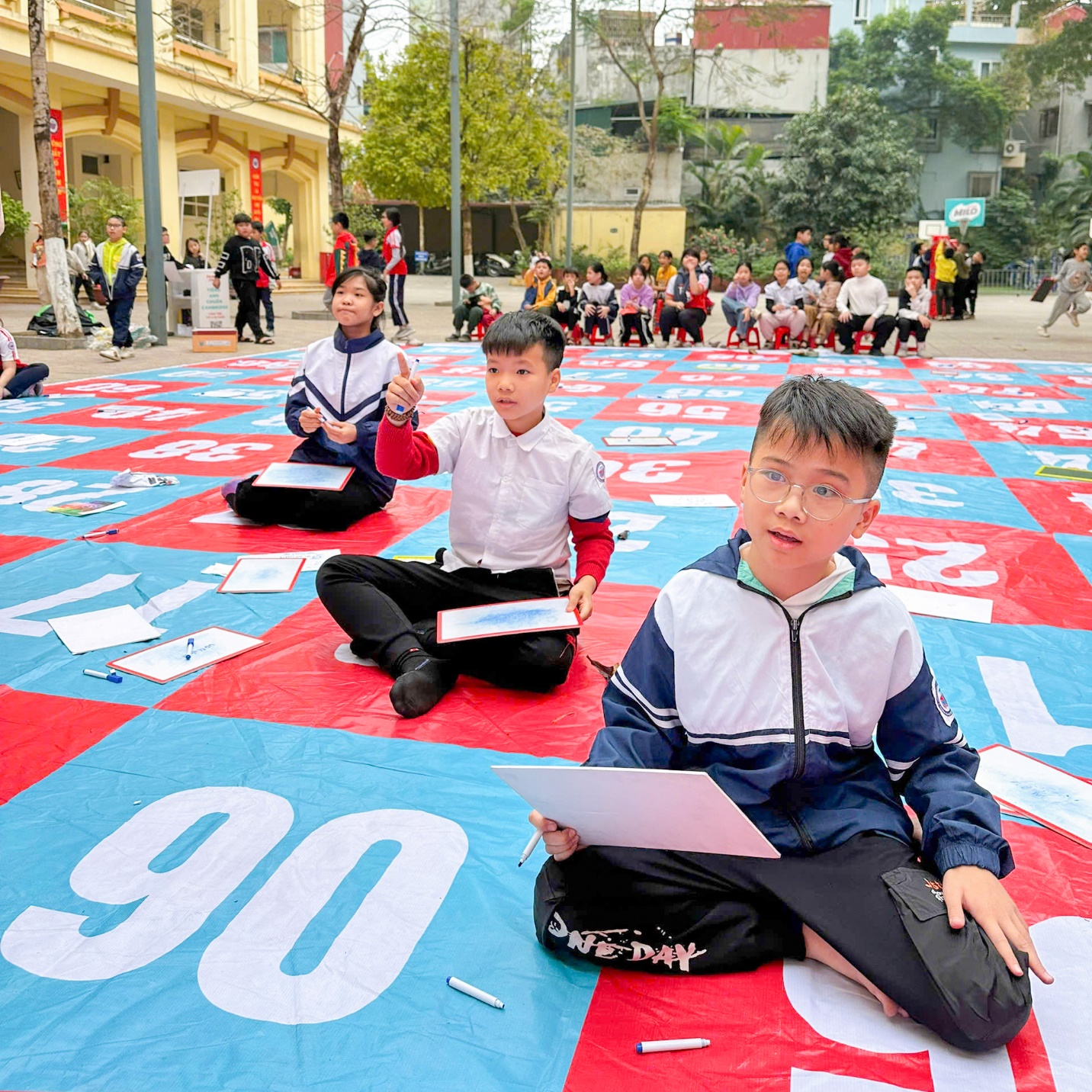 A group of people sitting on a red and blue blanket

Description automatically generated