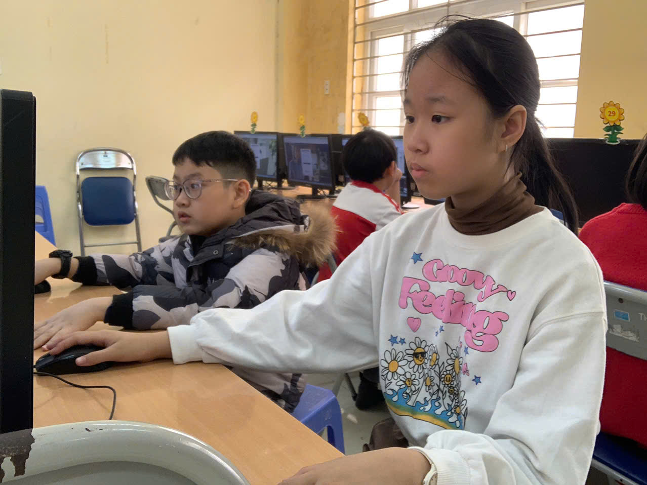 A group of children sitting at a table using computers

Description automatically generated