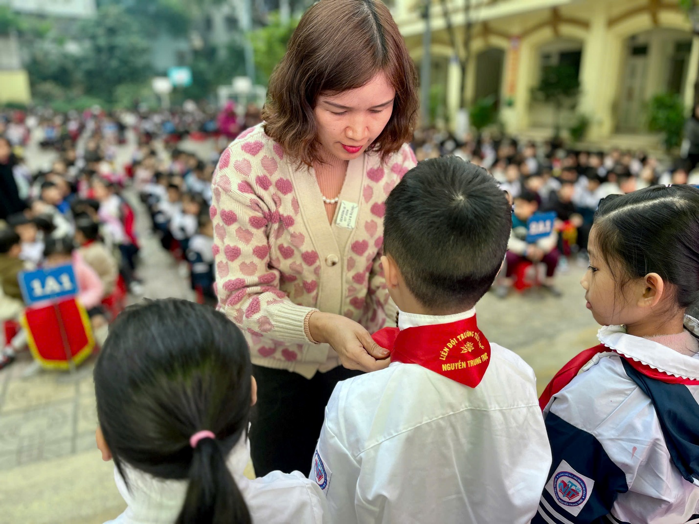 A person helping a child with a red ribbon around her neck

Description automatically generated