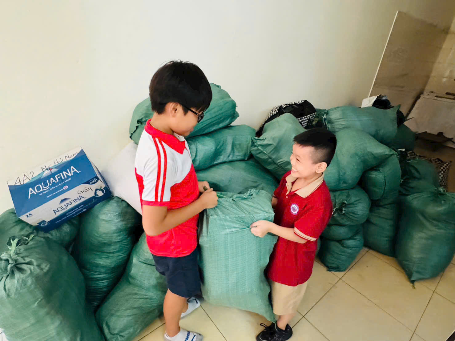 Two boys standing next to a pile of green bags
AI-generated content may be incorrect.
