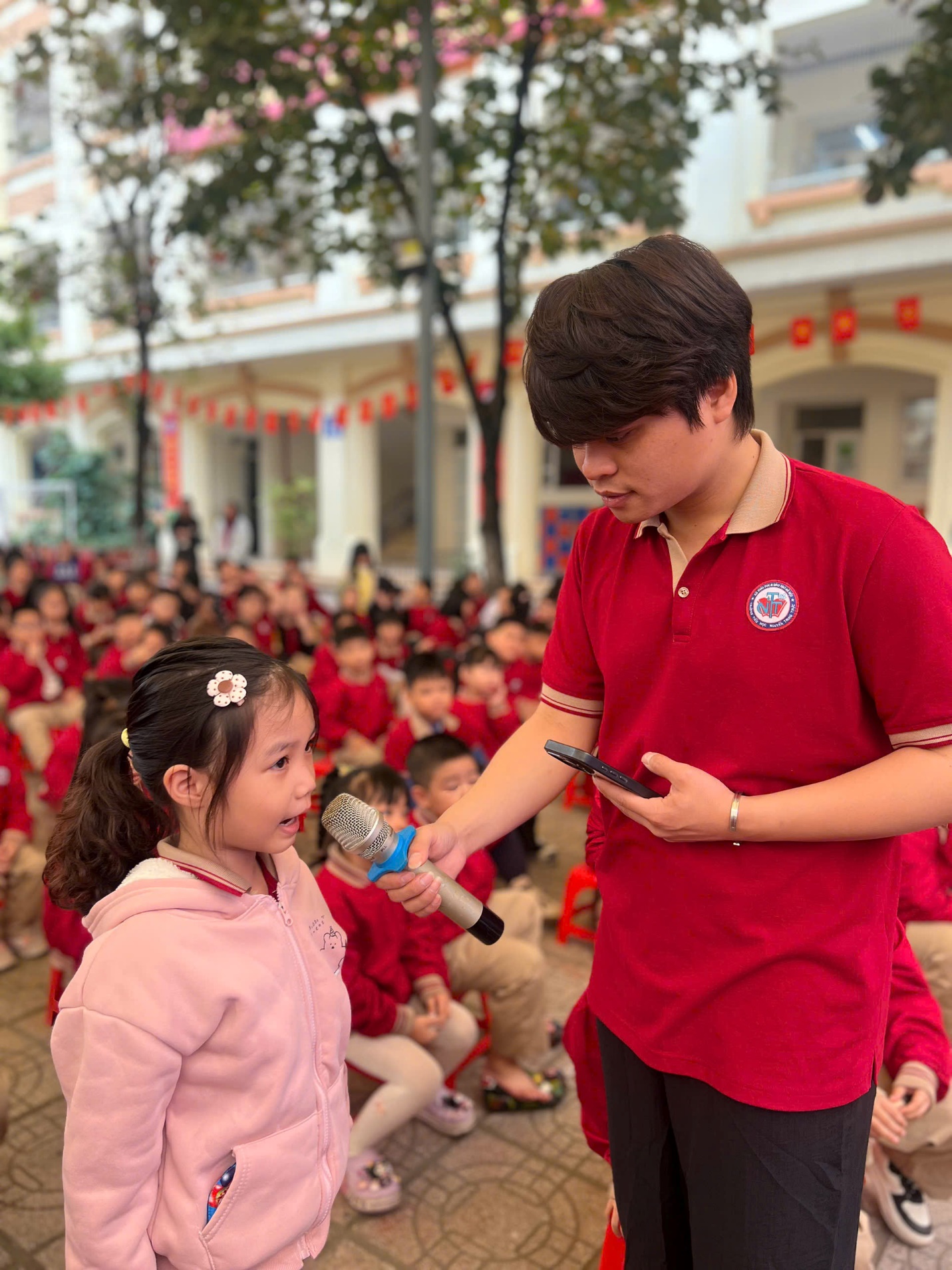 A person in red shirt holding a microphone to a child in front of a crowd

AI-generated content may be incorrect.