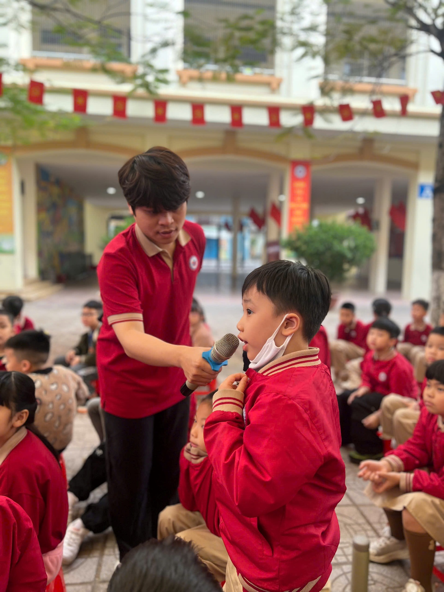 A person in red shirt holding a microphone to a child in a classroom

AI-generated content may be incorrect.