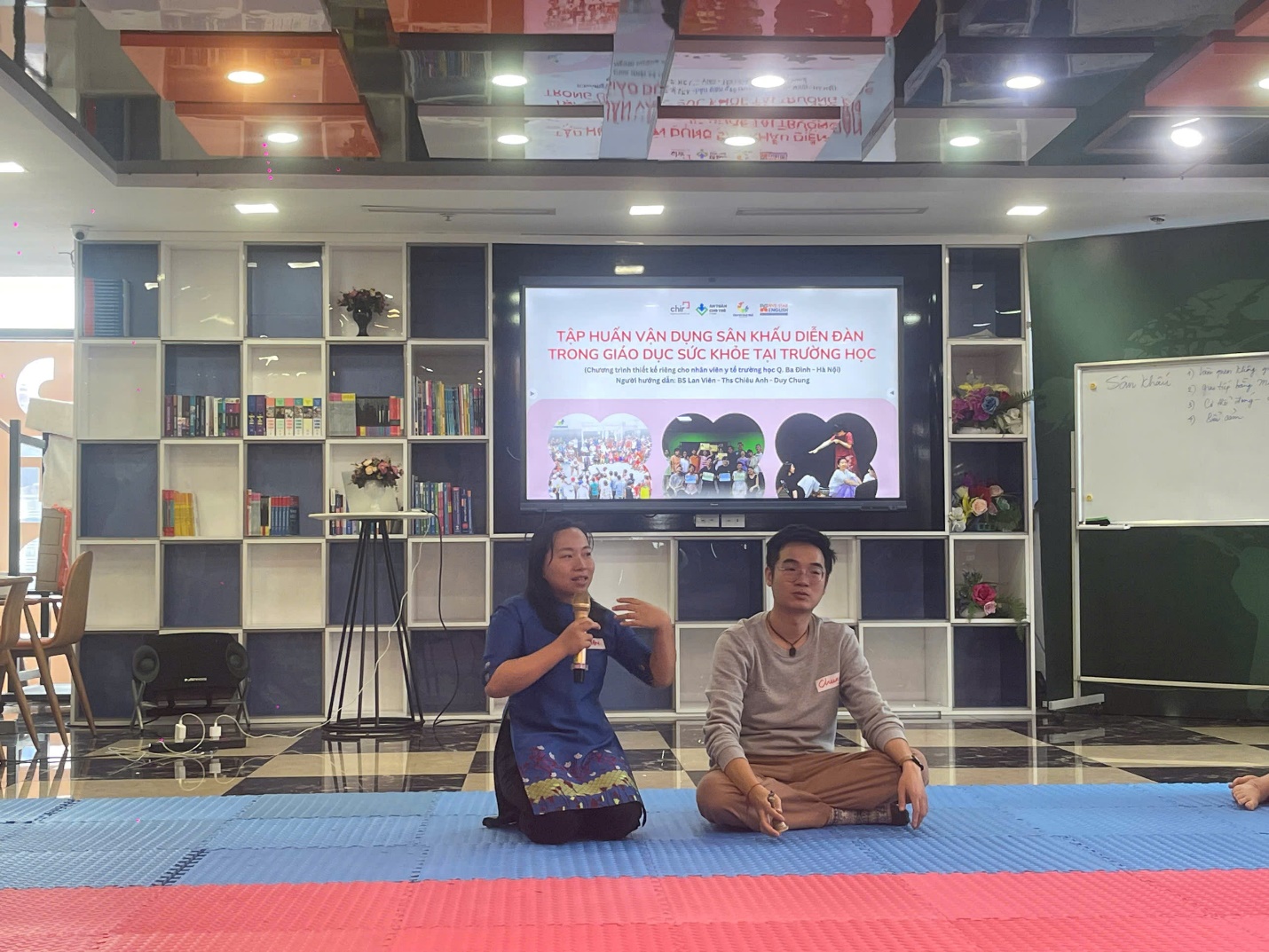 A person and person sitting on a blue mat in front of a screen

AI-generated content may be incorrect.