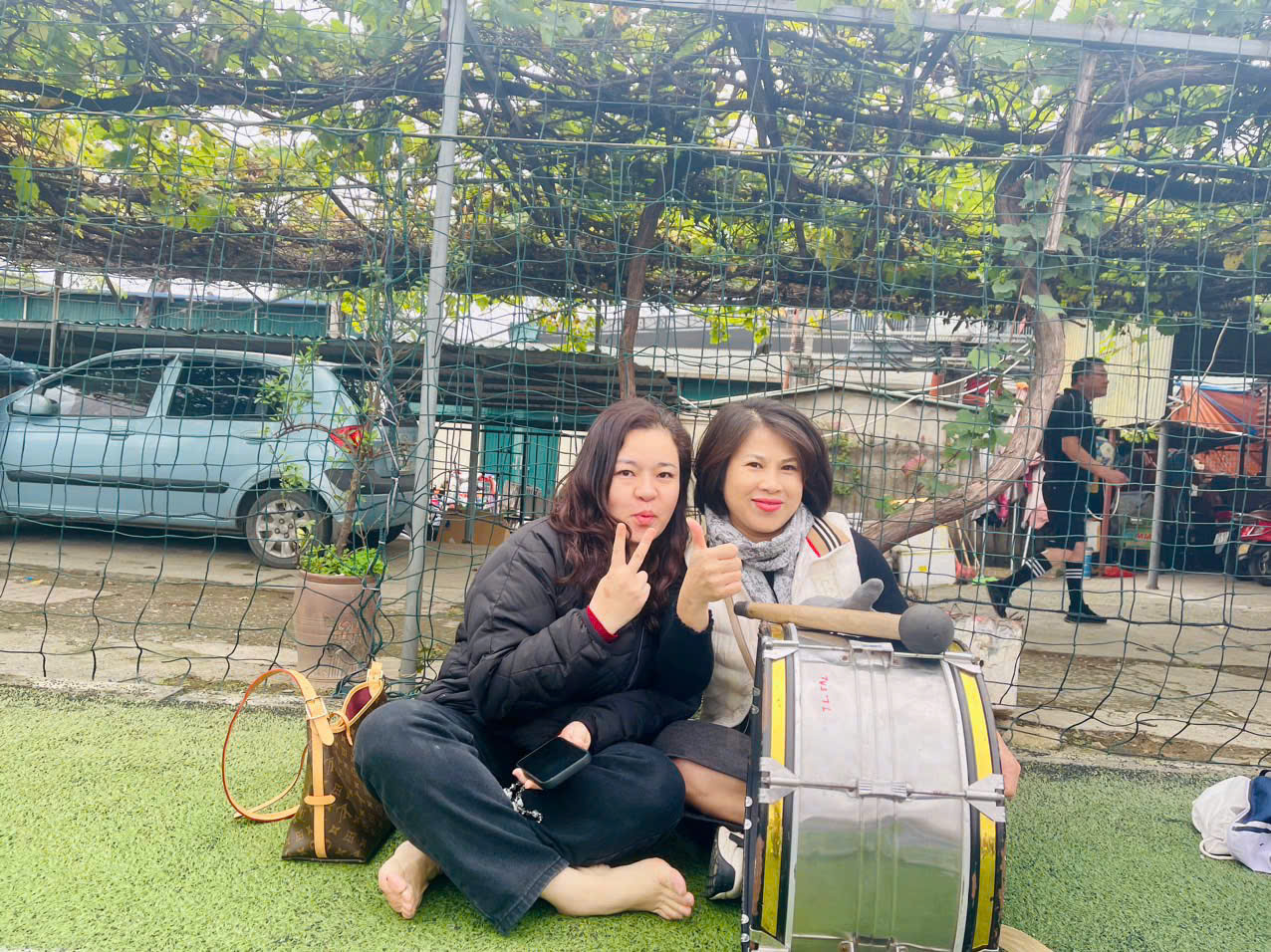 Two women sitting on the ground with a drum and a tree

AI-generated content may be incorrect.