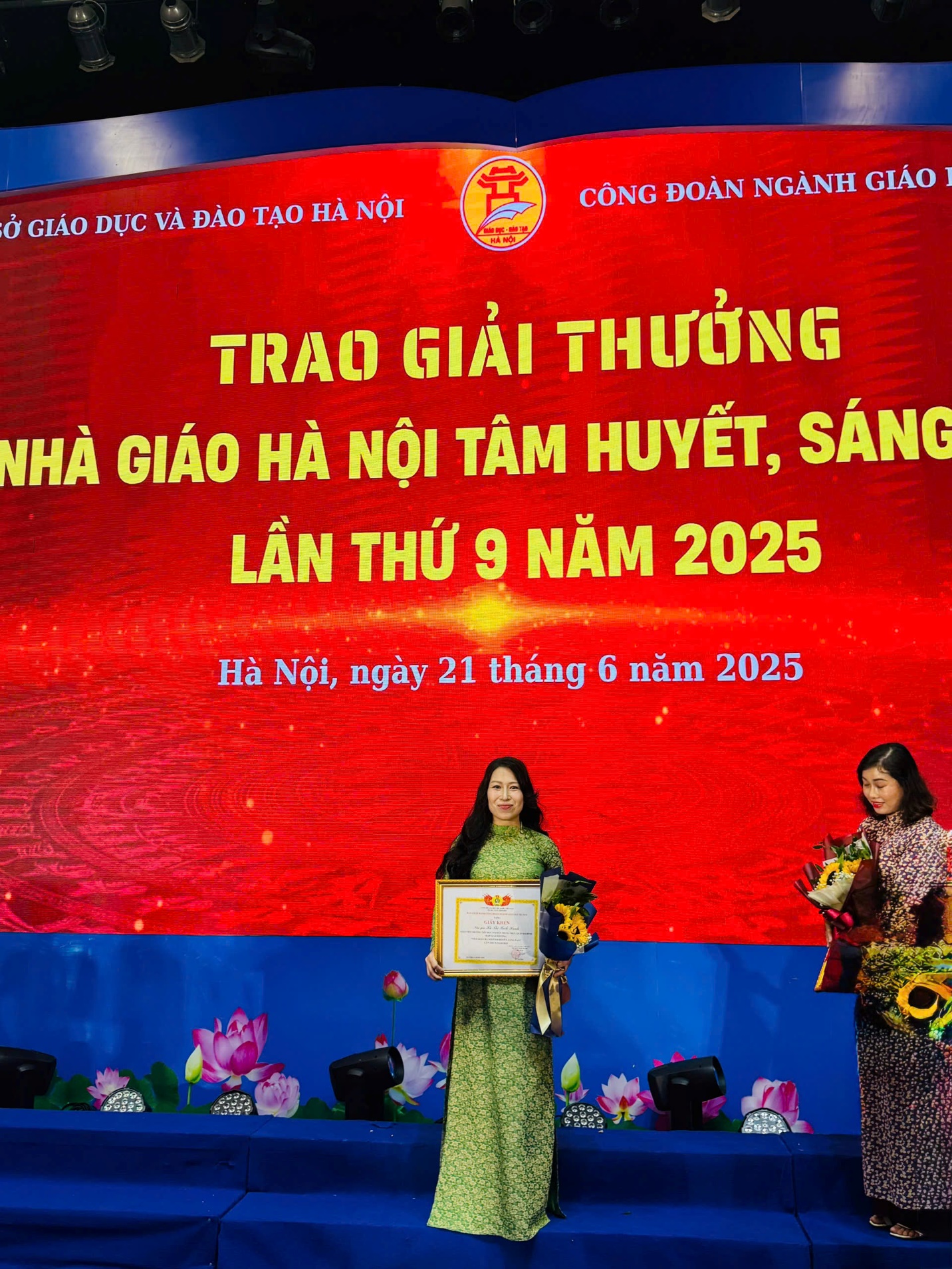 A person standing on a stage with a sign on the wall
AI-generated content may be incorrect.