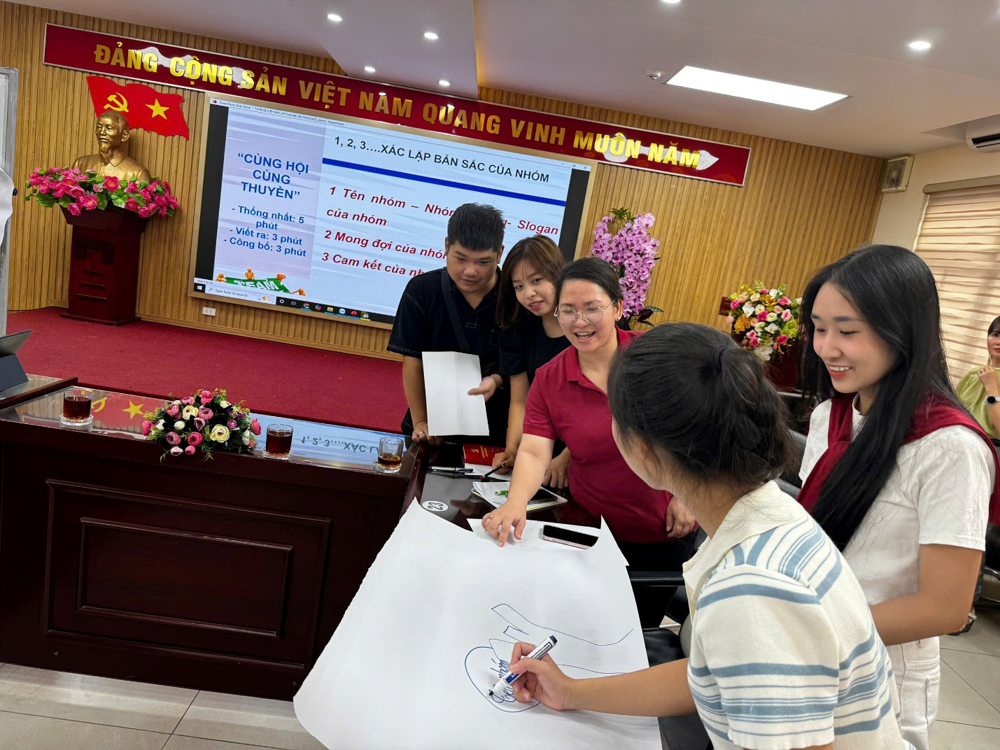 A group of people standing around a desk

AI-generated content may be incorrect.
