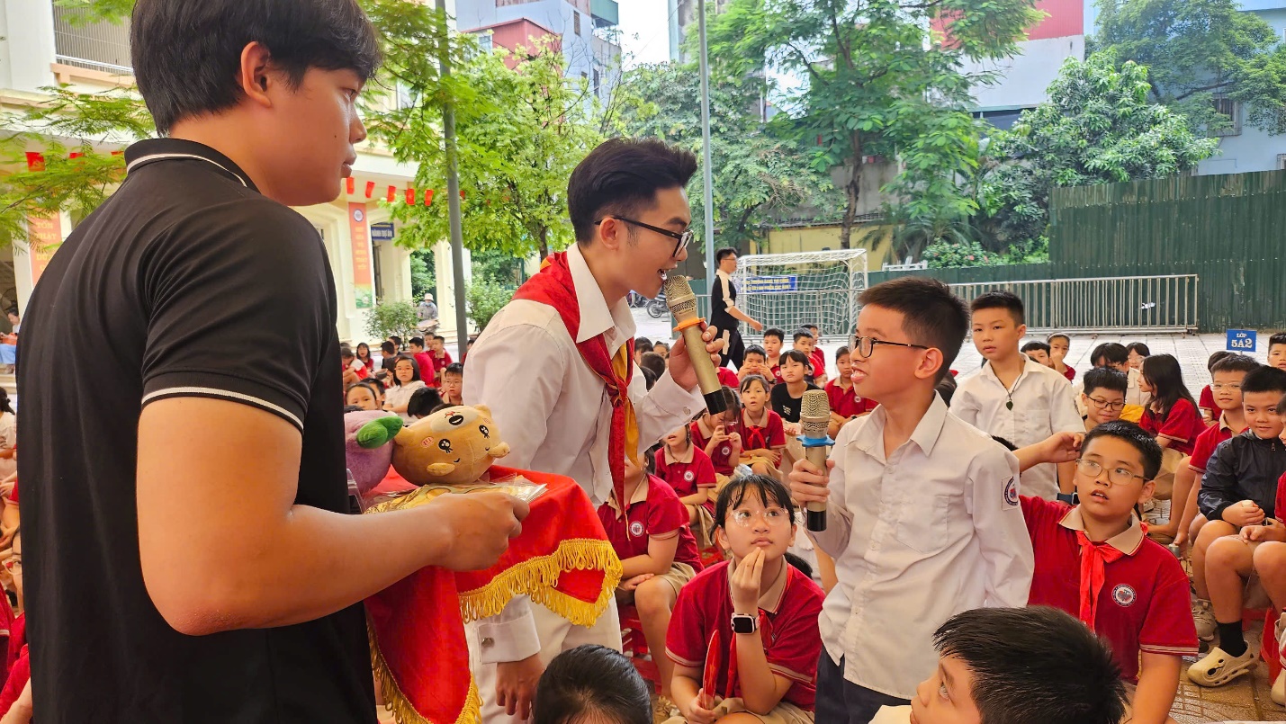 A person holding a microphone and speaking to a group of children

AI-generated content may be incorrect.