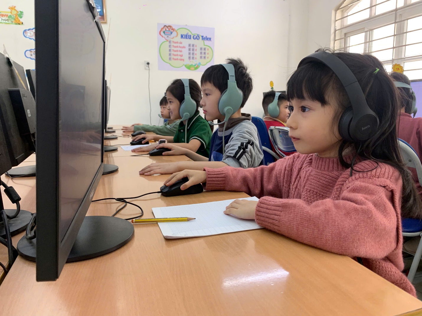 A group of children wearing headphones sitting at a desk with computers
AI-generated content may be incorrect.